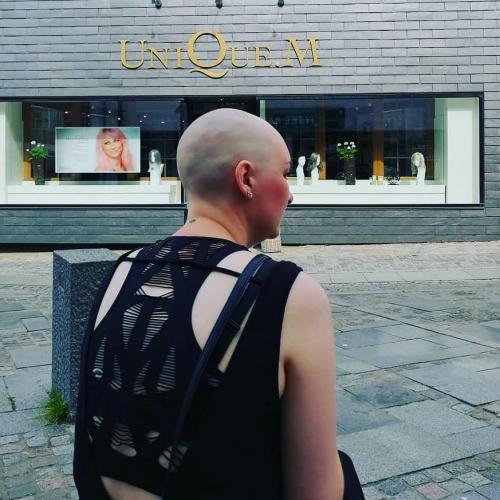 Susanne venter foran salonen. For første gang viser Susanne sig uden hår i det offentlige rum. En ny rejse er startet og den har været hel fantastisk.
